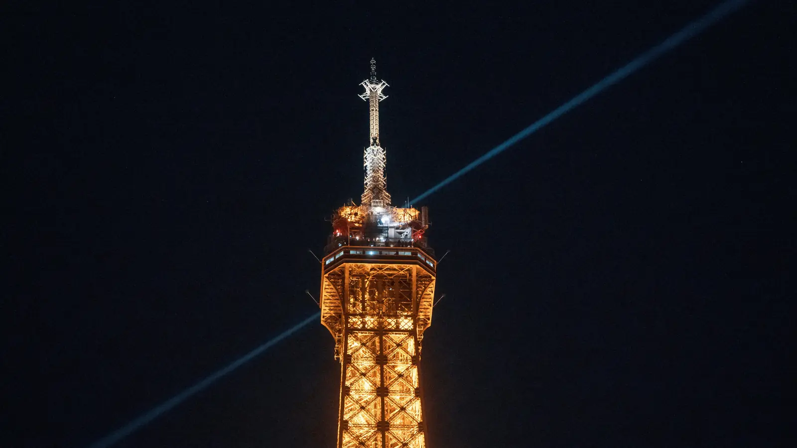 The illuminated top of the Eiffel Tower at night above Paris