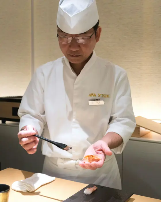 A sushi chef preparing a piece at the counter