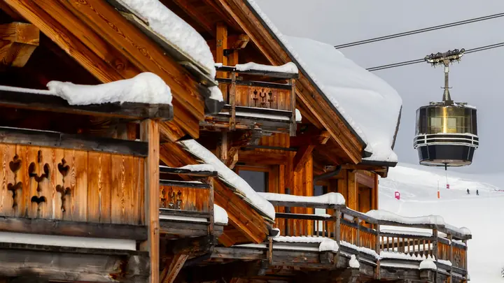 A wooden chalet under snow beside a cable car in the Alps